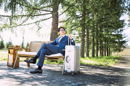 緑に囲まれたベンチで足を組むビジネスマン、海外出張中