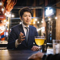 夜間の繁華街バーのテラス席で接待するビジネスマンの写真