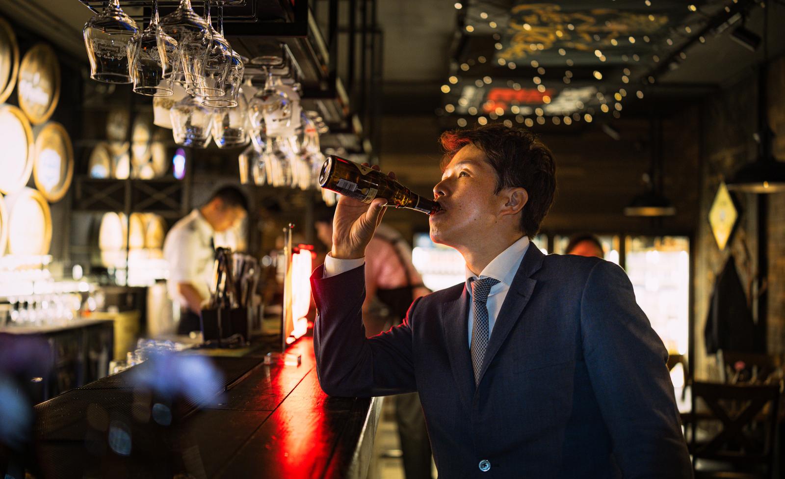 BARカウンターでビールを飲む濃紺スーツ姿の男性会社員［モデル：野崎繁裕］