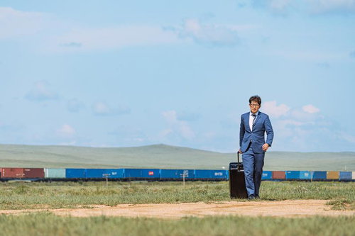 モンゴルの草原で貨物列車を背にスーツケースを引くビジネスマン