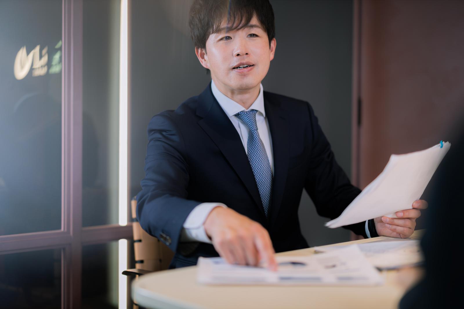 企業概要書を確認するスーツ姿のM&Aアドバイザー［モデル：野崎繁裕］