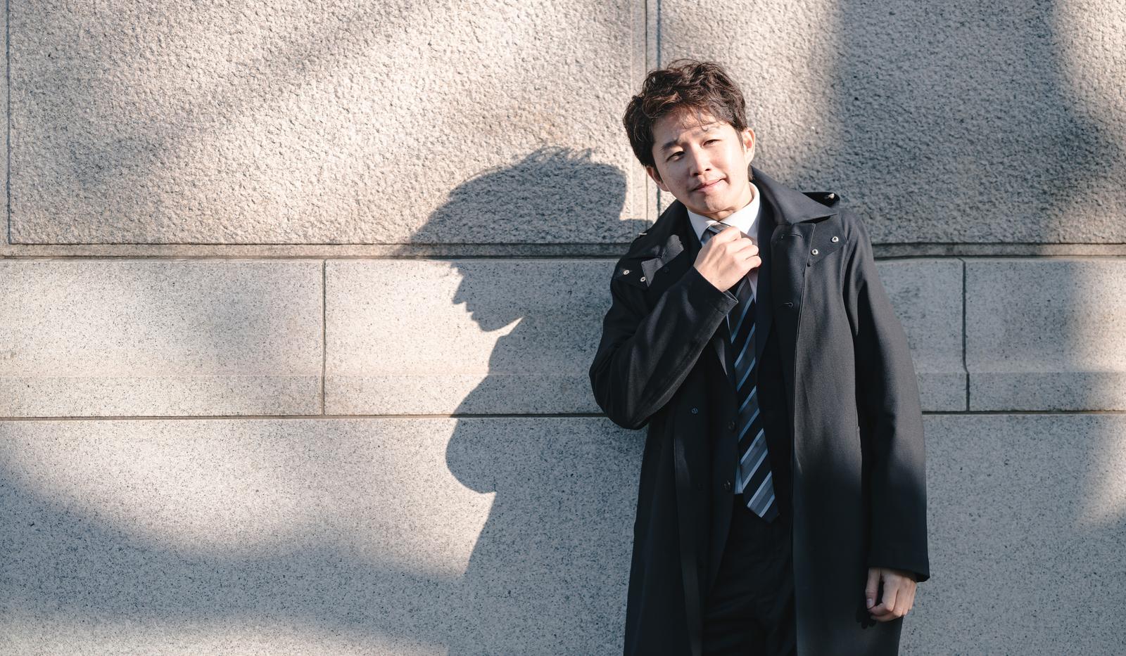 ネクタイを緩めて石壁にもたれる中年男性［モデル：野崎繁裕］