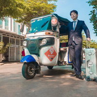 トゥクトゥクで出社するスーツ姿の男性とキャリーケースの写真