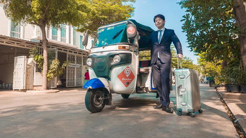 トゥクトゥクで出社するスーツ姿の男性とキャリーケース