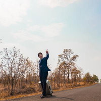 カンボジアの田舎道でキャリーケースを引くスーツ姿の営業マンの写真