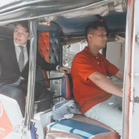 赤いポロシャツの運転手とスーツ姿の男性が乗るトゥクトゥクの写真