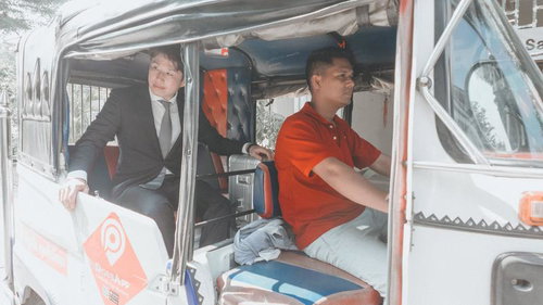 赤いポロシャツの運転手とスーツ姿の男性が乗るトゥクトゥク