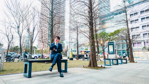 オフィス街のベンチで休憩する紺色スーツの男性ビジネスマン