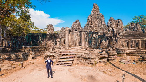 青空下のバイヨン遺跡でポーズを決めるネイビースーツの男性
