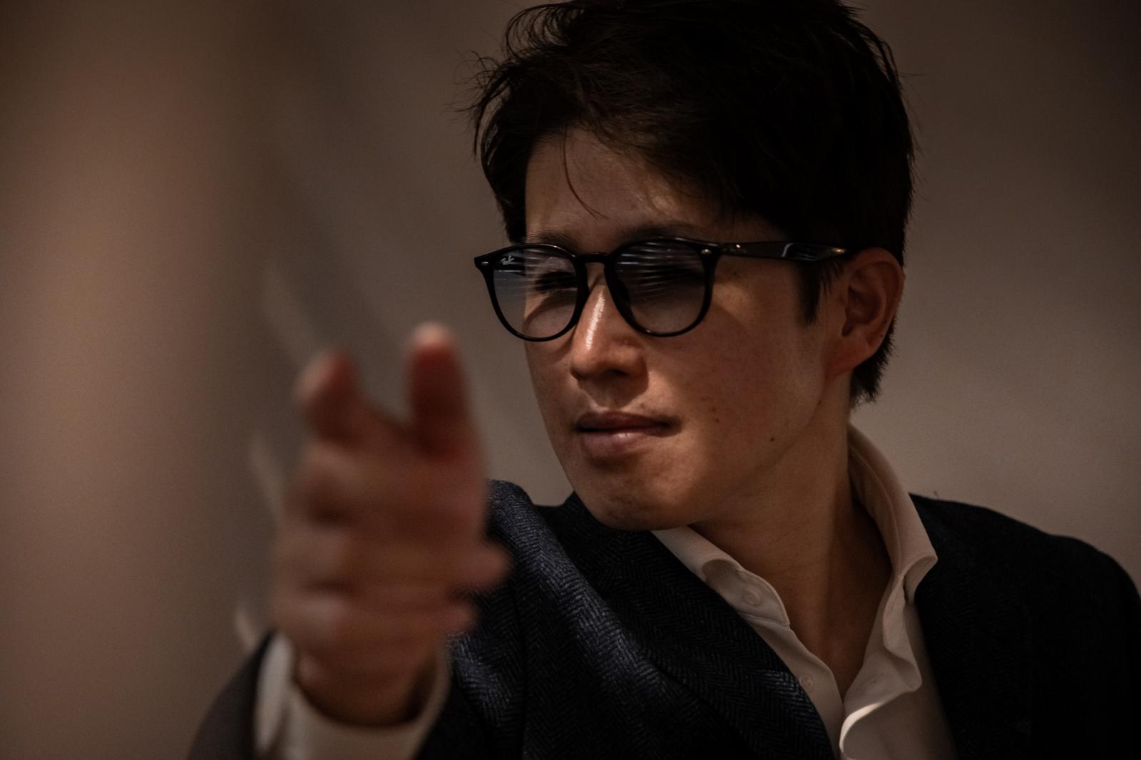 指を指すメガネをかけたビジネスマン［モデル：野崎繁裕］