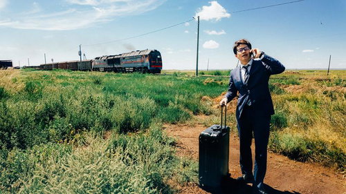 走り抜ける貨物列車を背に電話するビジネスマン