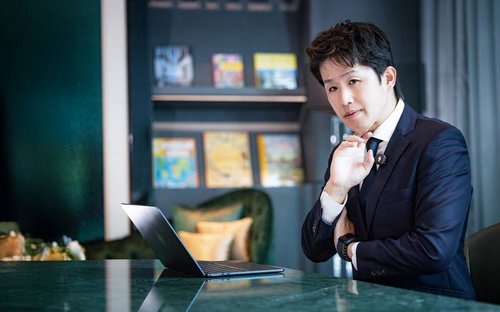 書棚のあるオフィスで頬杖をつき考え込むスーツ姿のビジネスマン