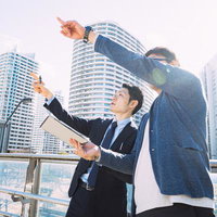 ビルを指して説明する建築視察中の会社員男性の写真