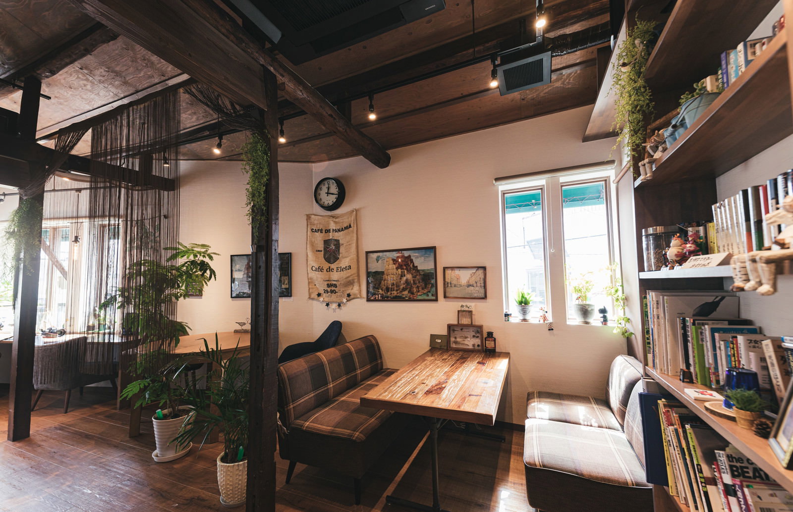 木材を多用した温かみのあるカフェ店内、本棚と観葉植物が配置
