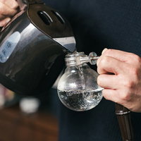 サイフォンにケトルで注ぐバリスタの手元、コーヒー抽出の準備作業の写真