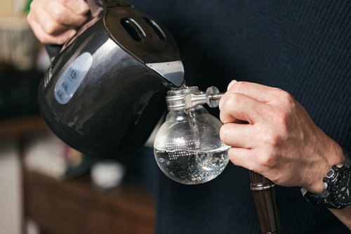 サイフォンにケトルで注ぐバリスタの手元、コーヒー抽出の準備作業