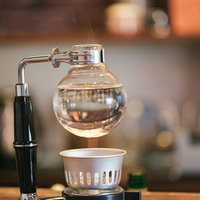 木製テーブルの上でサイフォン加熱中のコーヒー抽出風景の写真