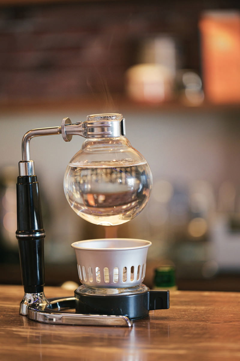 木製テーブルの上でガラス製サイフォンを使ってコーヒーを抽出している様子