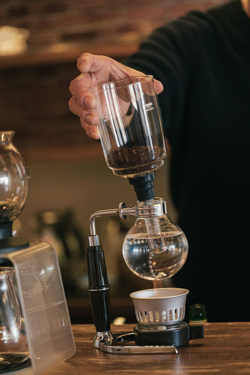 ガラス製サイフォンでコーヒーを淹れるバリスタの手元