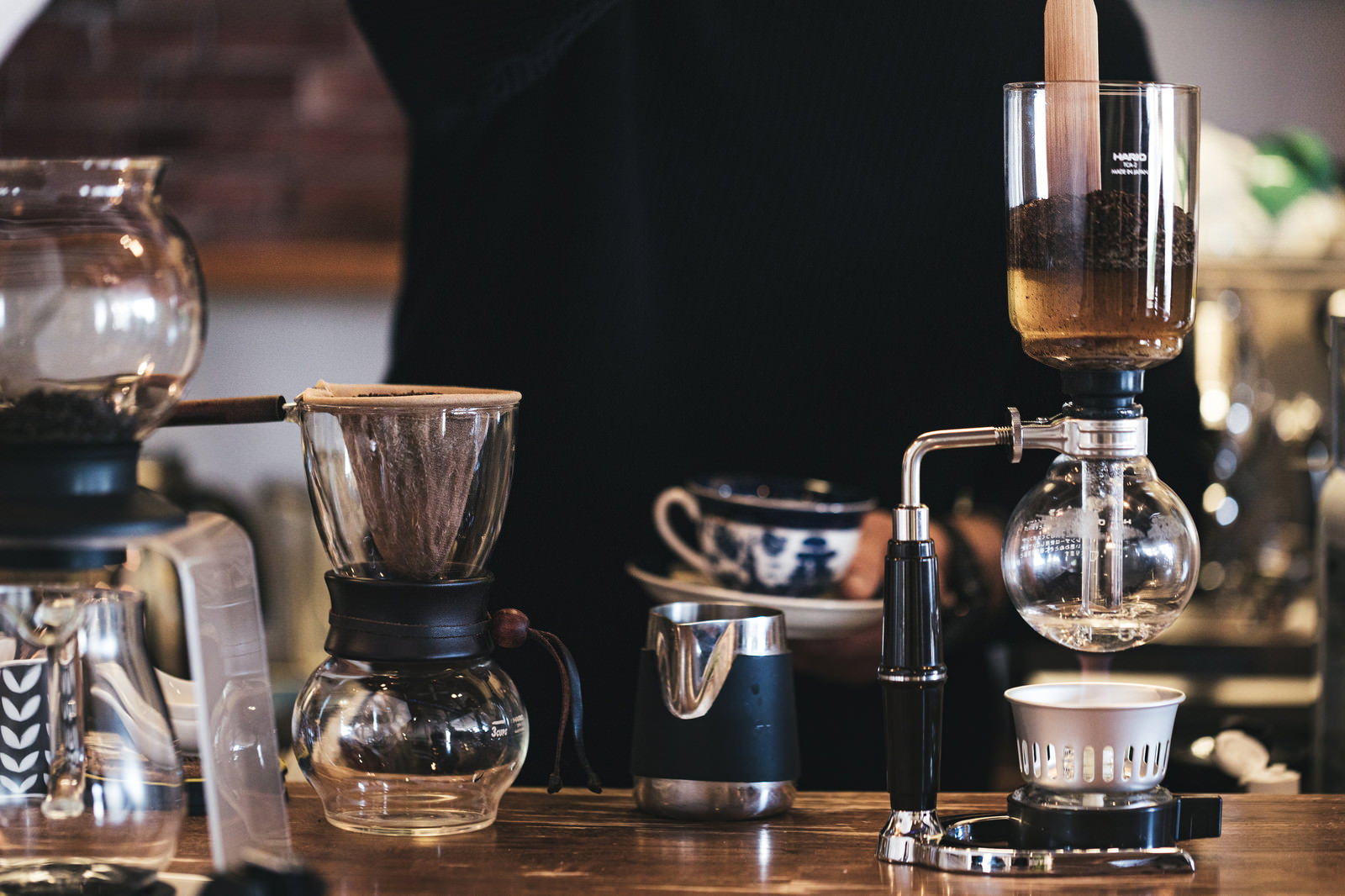木製カウンターに並ぶサイフォンやドリッパーなどのコーヒー器具