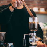 眼鏡をかけたカフェマスターがサイフォンでコーヒーを抽出中の写真