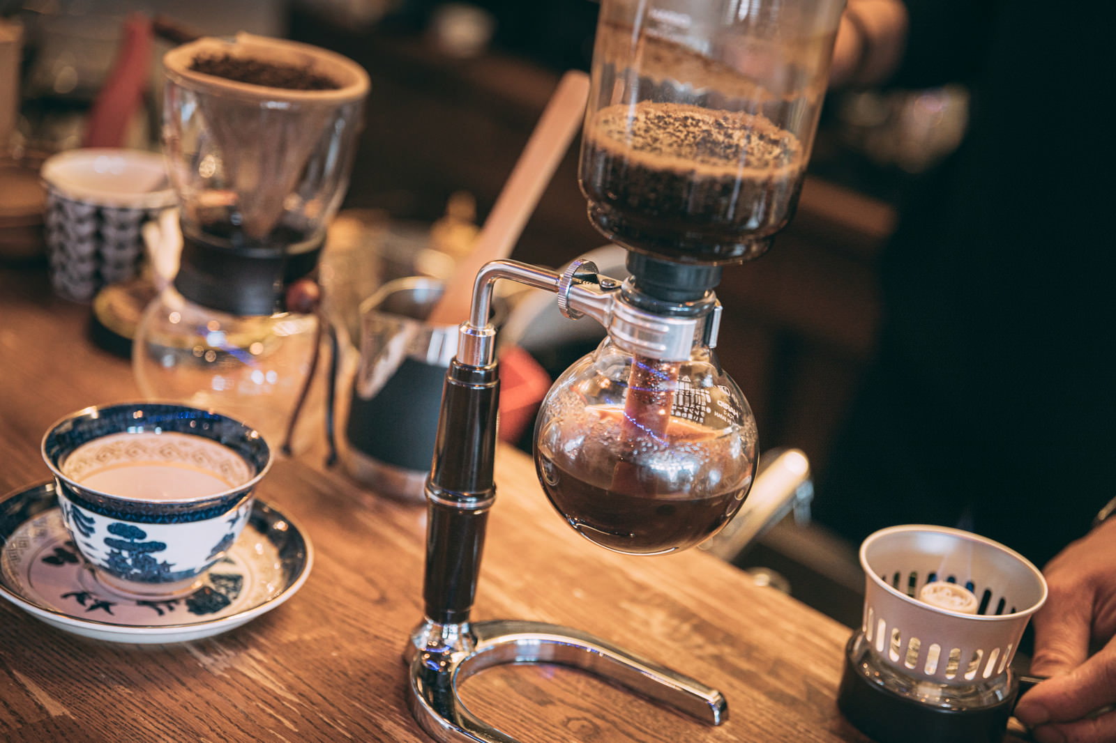 サイフォンを使ってコーヒーを淹れている手元とカップが並んだテーブル