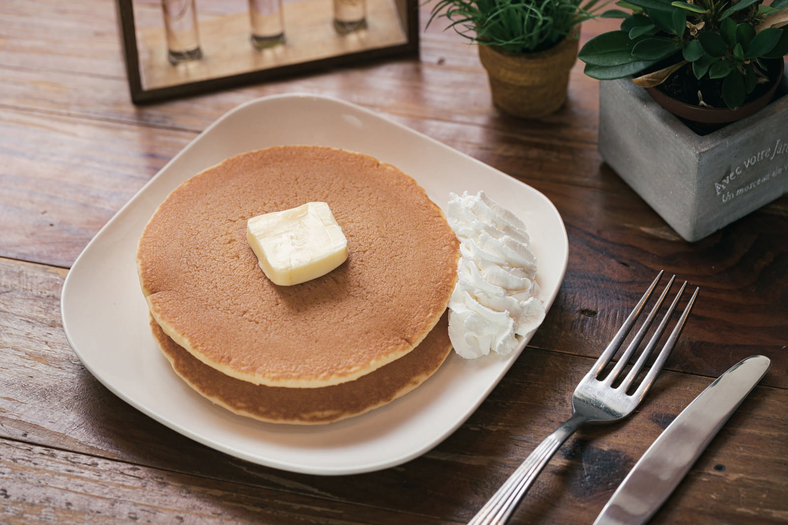 木目のテーブルに置かれた白い皿の上のパンケーキにバターとホイップクリーム