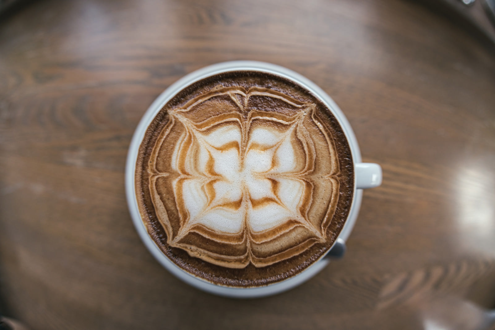 白いカップに花模様のラテアートが描かれたコーヒー