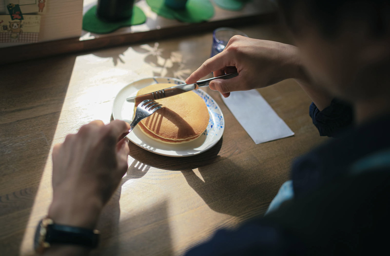 フォークでホットケーキを切り分ける手元と皿に盛られた生クリーム