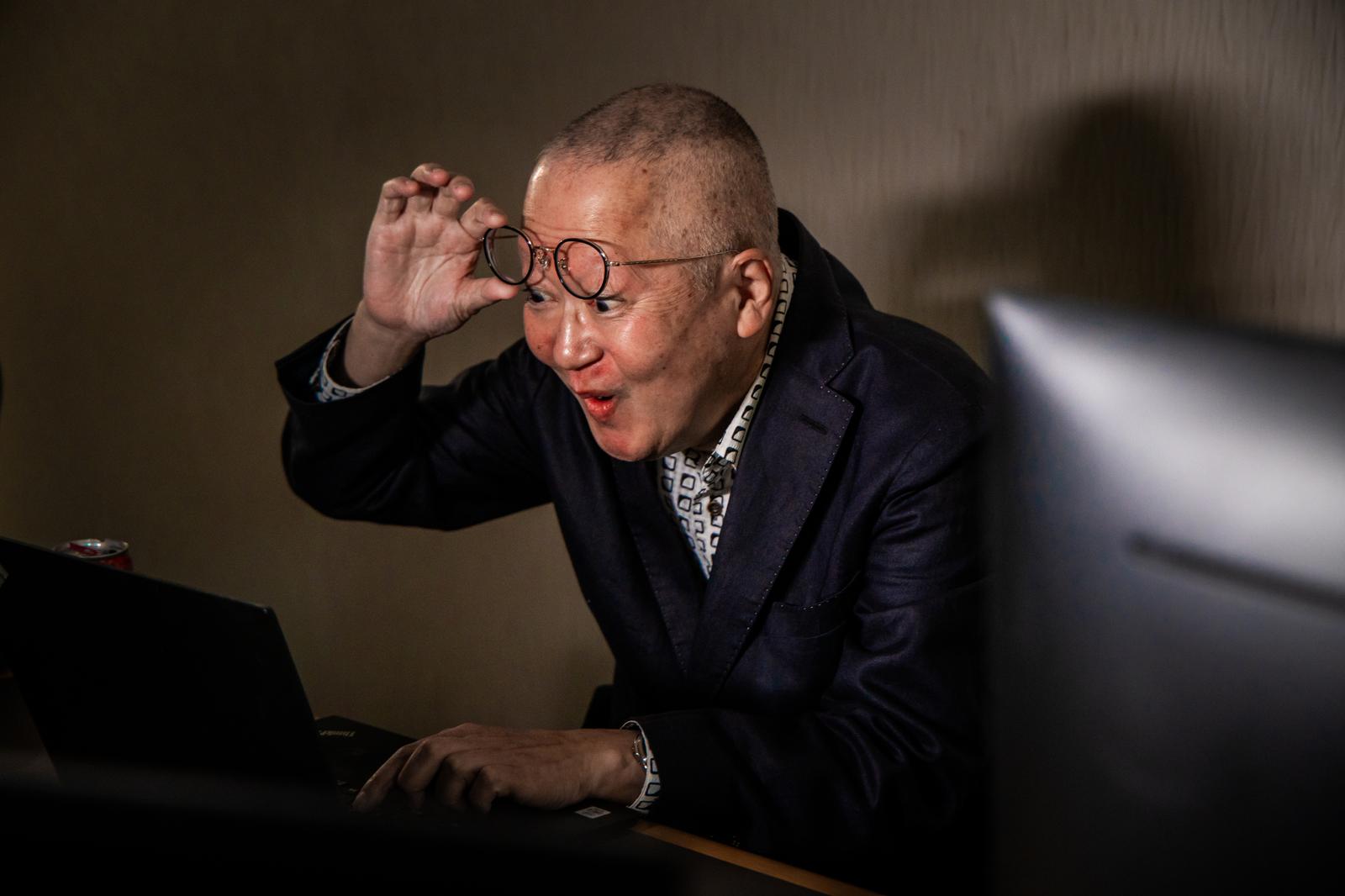 VRゴーグルを装着する紺色ジャケット姿の高齢男性がノートパソコンの前に座っている［モデル：渡辺カンジ］