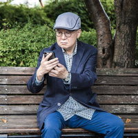 お返事まだカナ？公園でスマホを見るシニア男性の写真
