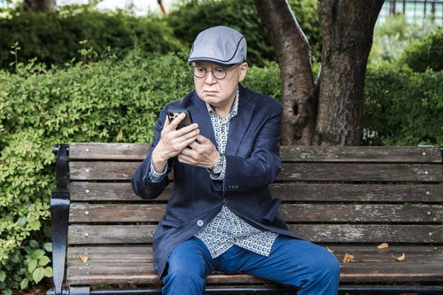 お返事まだカナ？公園でスマホを見るシニア男性