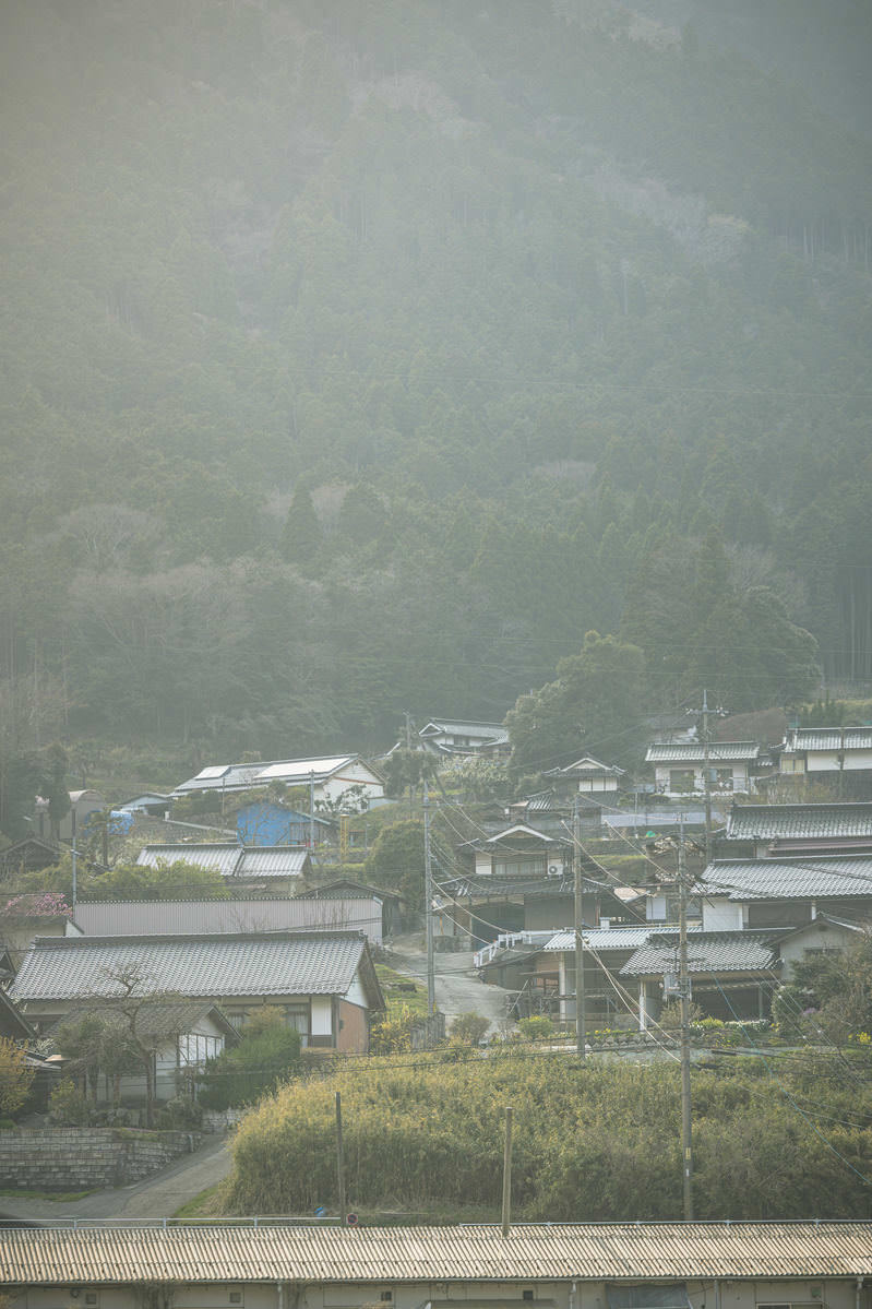 霧が立ちこめた山間にある瓦屋根の民家が立ち並ぶ田舎町の風景