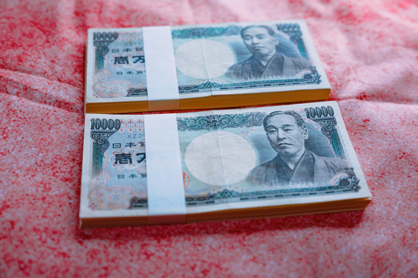 帯巻きされた1万円札の札束2本がピンク色の布の上に置かれている