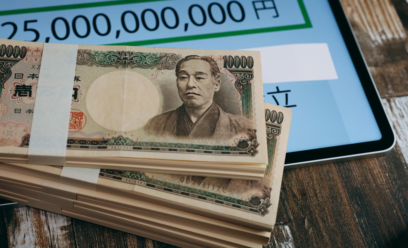 金額表示のあるタブレット画面と積み重ねた1万円札の札束