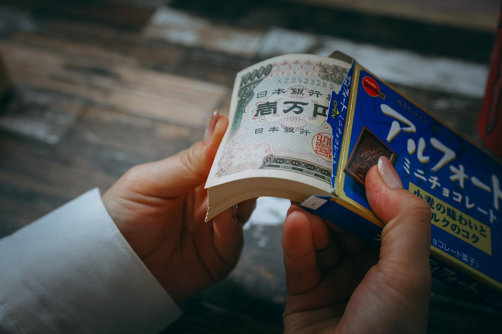 手に持った一万円札と青い箱の商品が机の上に置かれている様子