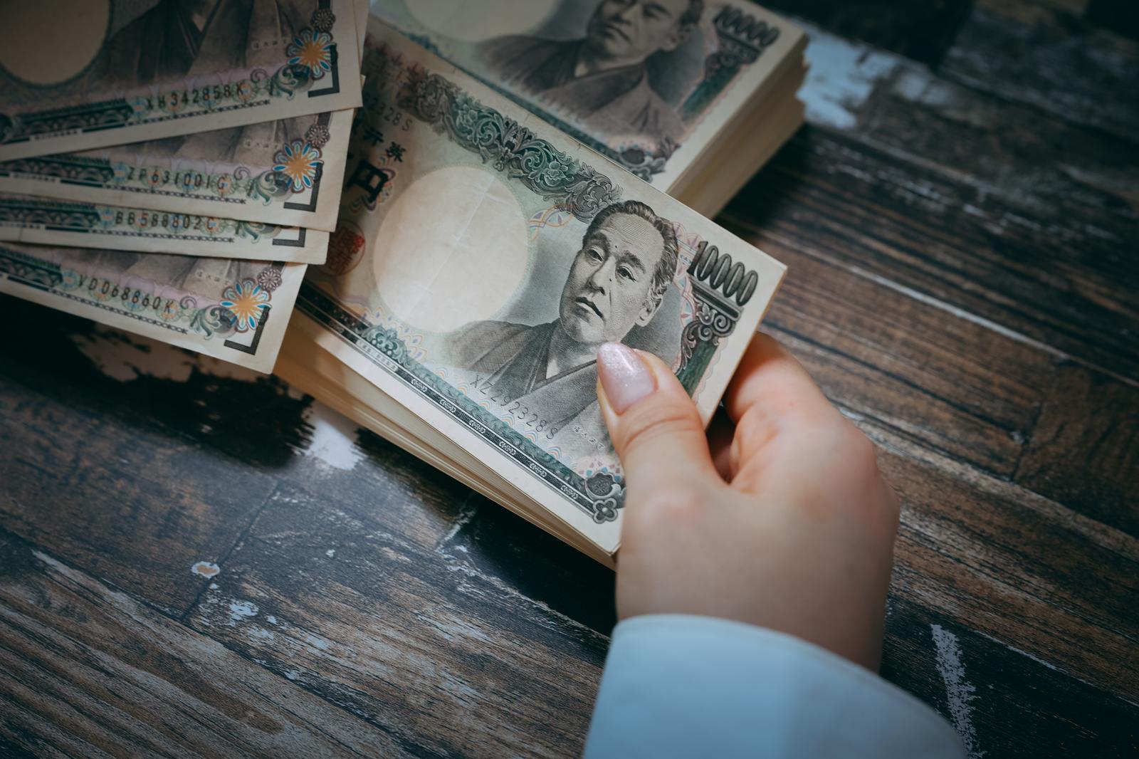 木製テーブルの上に積み重ねた札束を手で数える人物