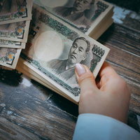 お金配ります系詐欺風、木製テーブルで札束を数える手の写真