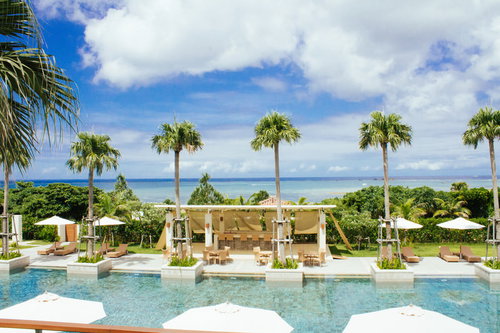 沖縄の青い海を背景にしたリゾートプールとヤシの木が並ぶ風景