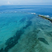 沖縄の離島に建つ白い灯台と海岸風景、青空と透明な海の写真