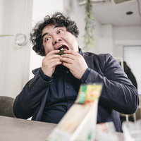 大口を開けておにぎりを食べる男性、オフィスでの昼食の写真