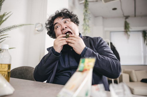 大口を開けておにぎりを食べる男性、オフィスでの昼食