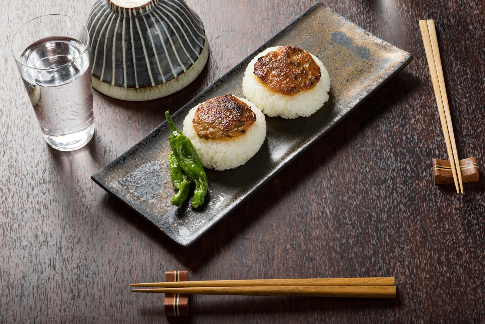 白い長皿に盛られた味噌焼きおにぎり2個とししとう、箸と徳利が配置された和食の夜食