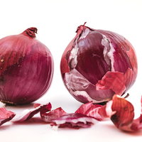 皮を剥いたレッドオニオンと散らばった薄い表皮の写真