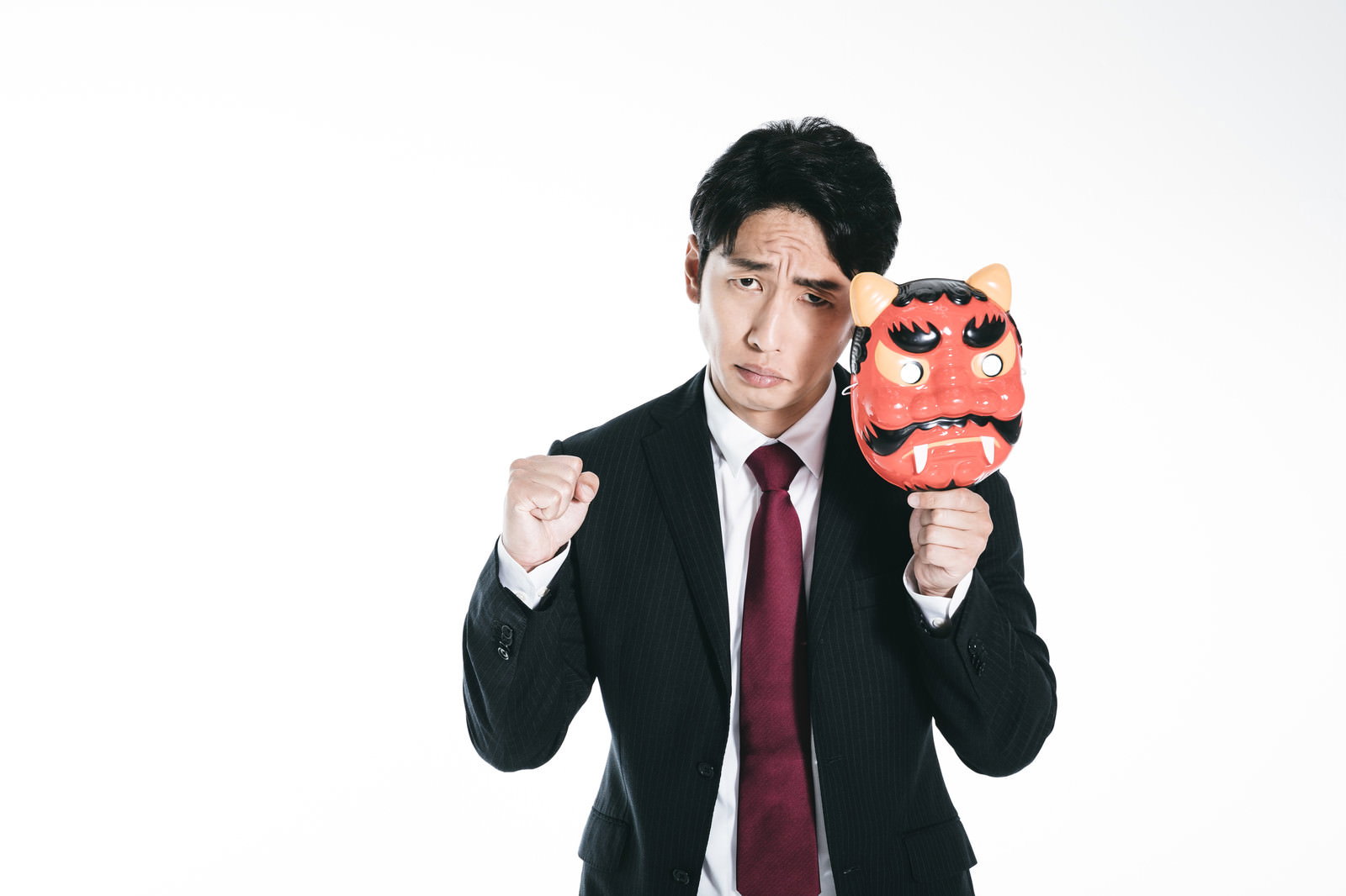 鬼の面を付けてファイティングポーズを取るスーツ姿の男性［モデル：大川竜弥］