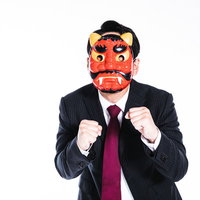 鬼の面をつけたスーツ姿の男性がファイティングポーズを取るの写真