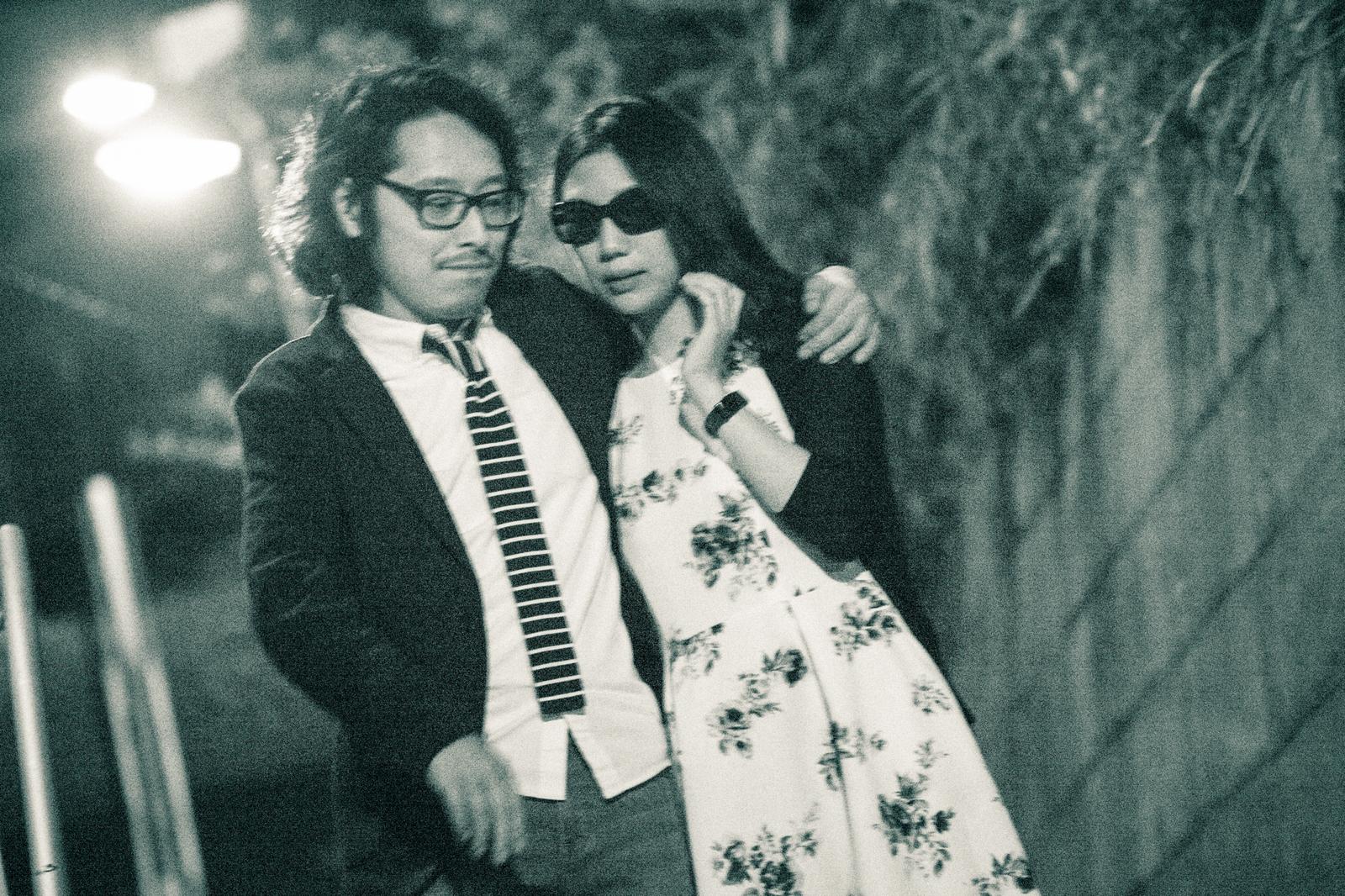 夜の街で肩を寄せ合う眼鏡の男性とサングラスの女性［モデル：ゆうせい］
