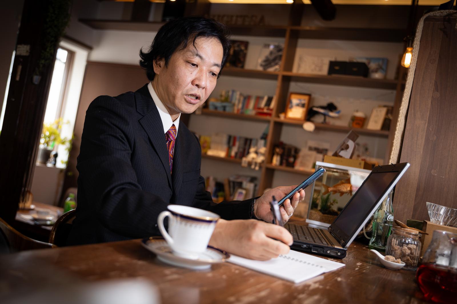 カフェでノートにメモを取るスーツ姿の男性［モデル：のせさん］