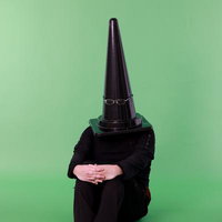 グリーンバックの前で体育座りする、カラーコーンを頭に被った人物の写真