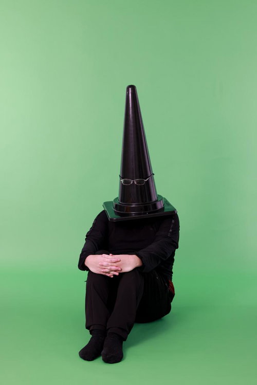 グリーンバックの前で体育座りする、カラーコーンを頭に被った人物